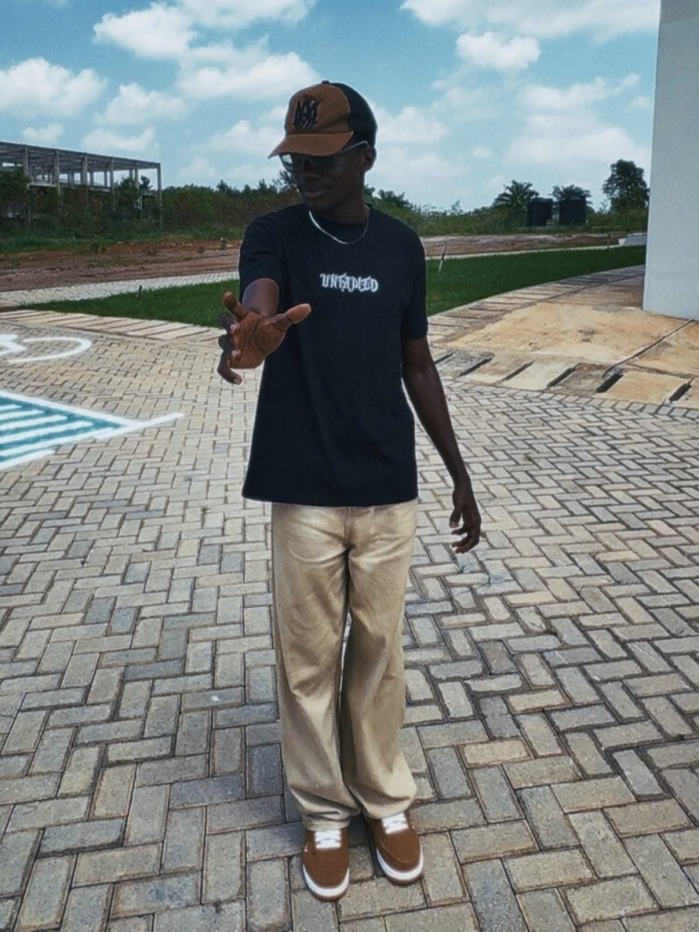 A young male wearing the black colorway of the Untamed Tee from DripAfrika with a trucker hat